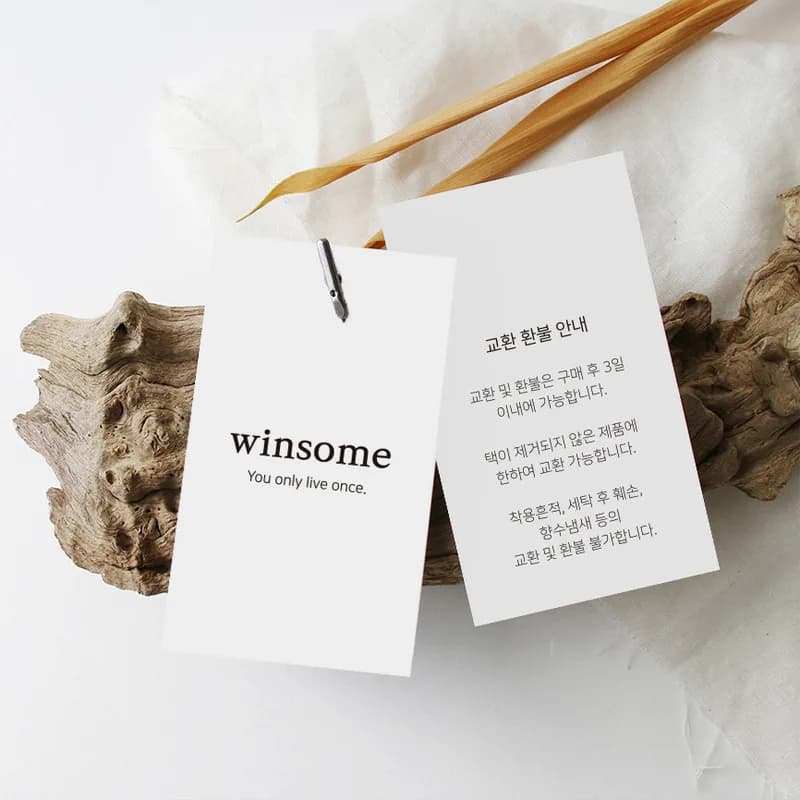 돌 위에 놓인 흰색 의류 행택 두 장의 앞뒤 실물 사진